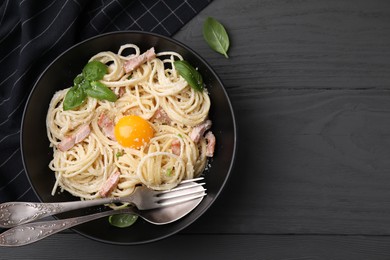 Bowl of delicious pasta Carbonara with egg yolk and cutlery on black wooden table, flat lay. Space for text