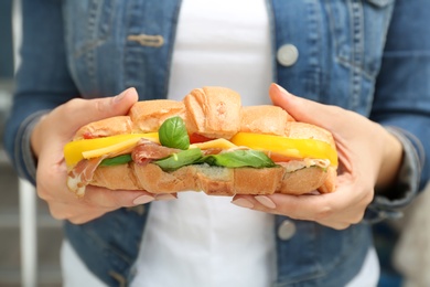 Photo of Woman holding tasty croissant sandwich, closeup