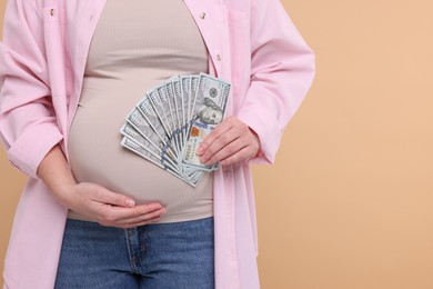 Photo of Surrogate mother. Pregnant woman with dollar banknotes on beige background, closeup. Space for text