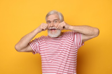 Senior man touching mustache on orange background