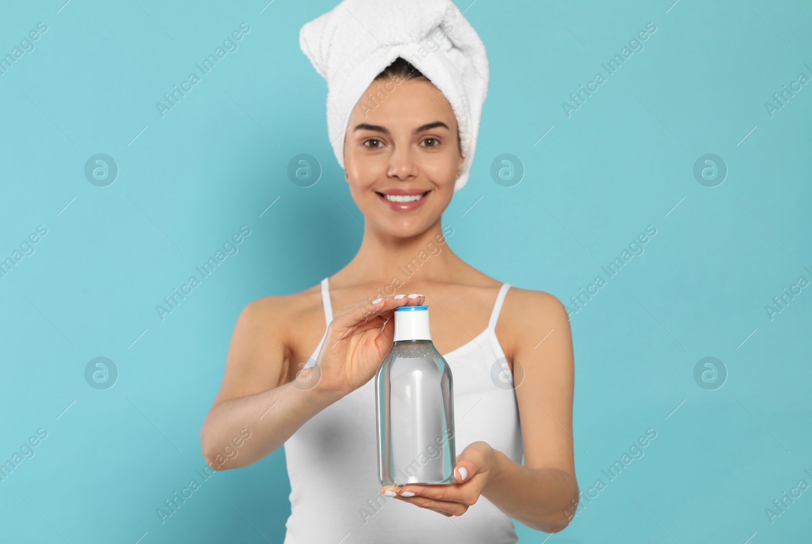 Photo of Young woman with bottle of micellar water on light blue background