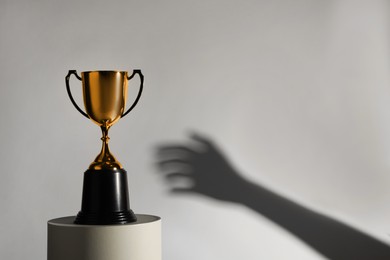 Photo of Woman reaching for gold trophy cup on light background, closeup