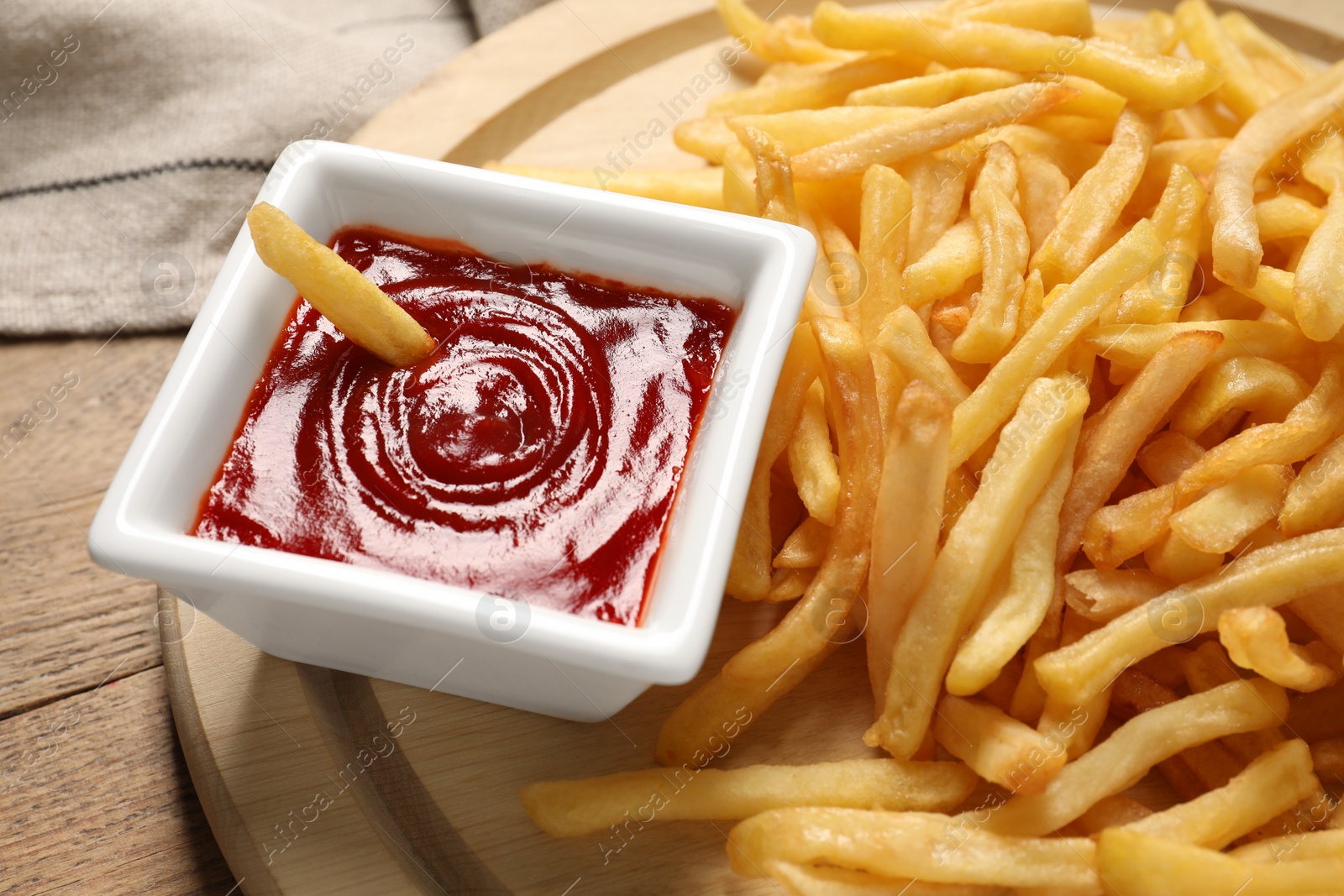 Photo of Board with tasty ketchup and fries on wooden table, closeup