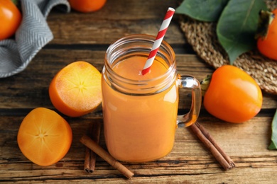 Photo of Tasty persimmon smoothie with straw and fresh fruits on wooden table