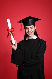 Happy student with graduation hat and diploma on red background