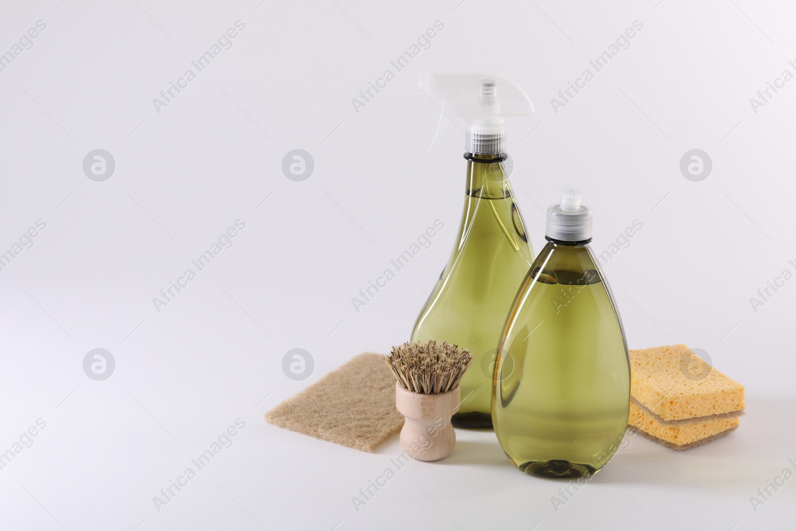 Photo of Bottles of cleaning product, brush and sponges on white background