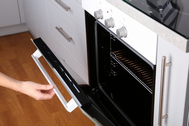 Photo of Woman opening electric oven in kitchen, closeup