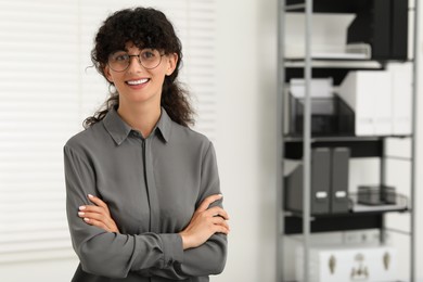 Photo of Portrait of confident businesswoman with crossed arms indoors. Beautiful lady in glasses smiling and looking into camera. Space for text
