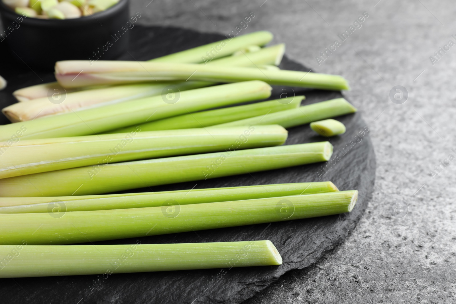 Photo of Slate board with fresh lemongrass stalks on grey table, closeup