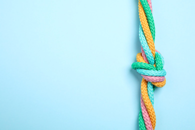 Photo of Top view of colorful ropes tied together on light blue background, space for text. Unity concept