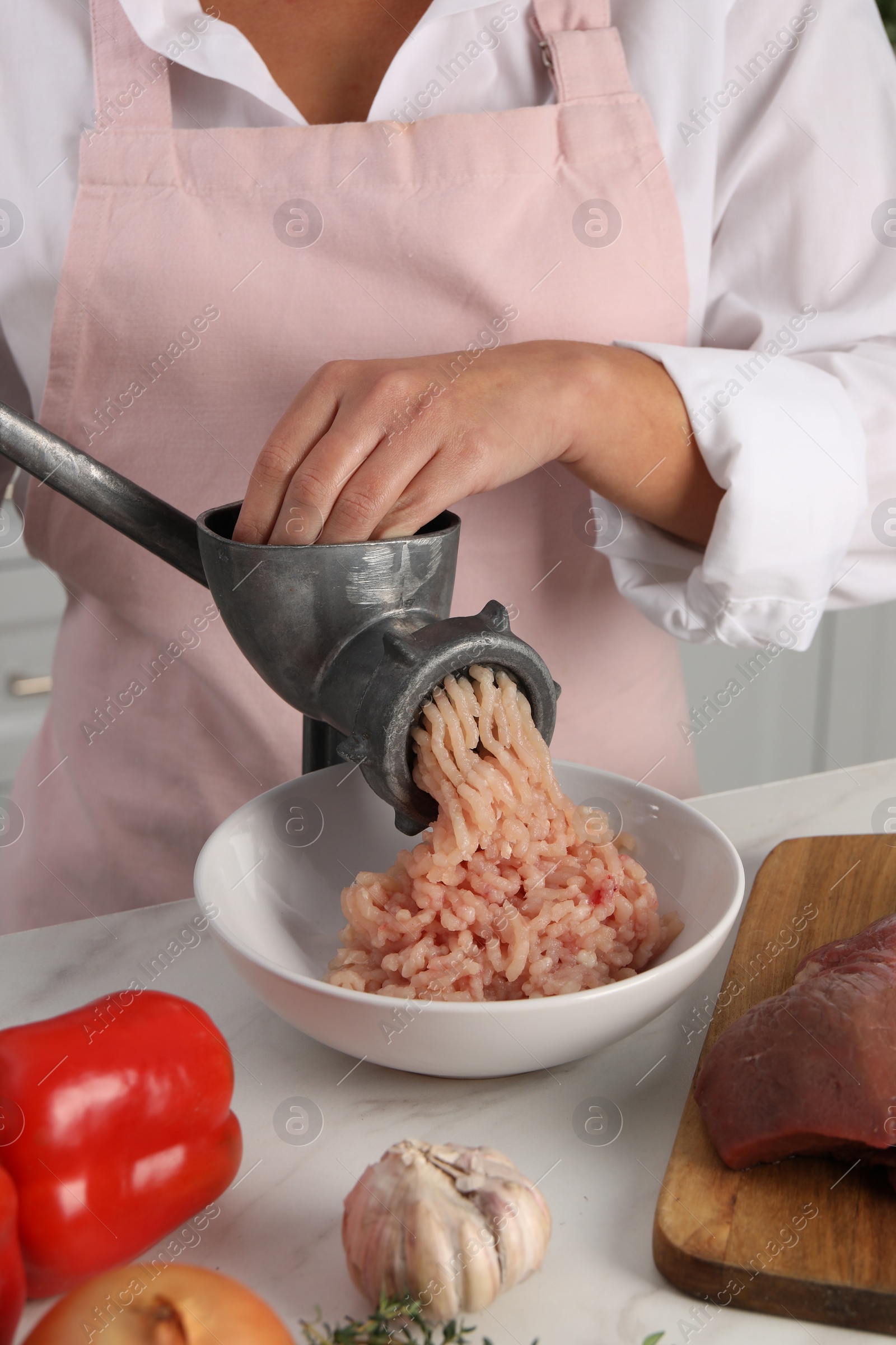 Photo of Woman making chicken mince with metal meat grinder at white table in kitchen, closeup