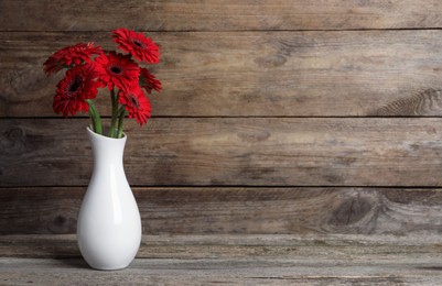 Photo of Bouquet of beautiful red gerbera flowers in ceramic vase on wooden table. Space for text