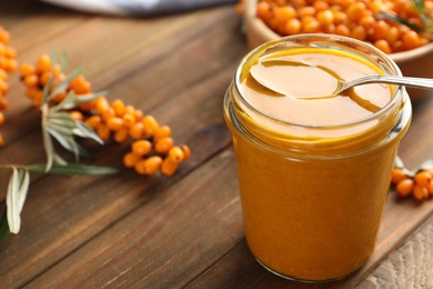 Photo of Delicious sea buckthorn jam and fresh berries on wooden table. Space for text