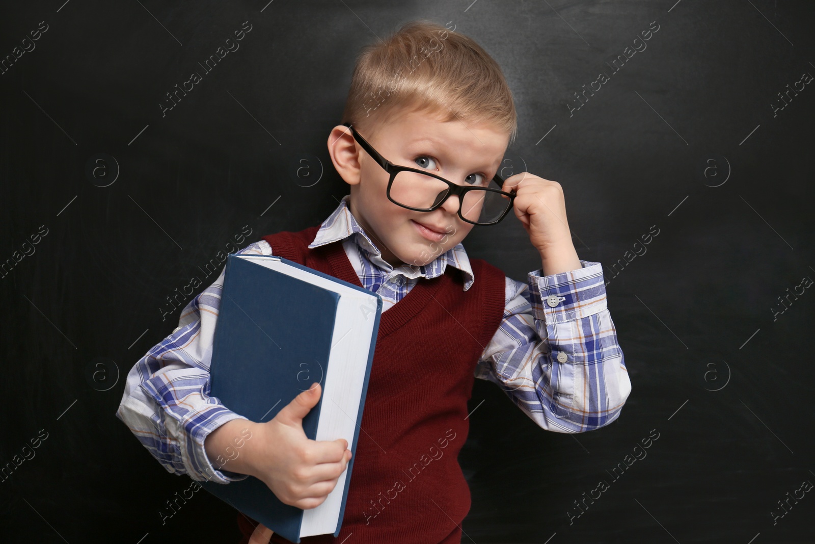 Photo of Cute little child wearing glasses near chalkboard. First time at school