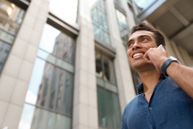 Photo of Portrait of handsome young African-American man talking on mobile phone outdoors, low angle view. Space for text