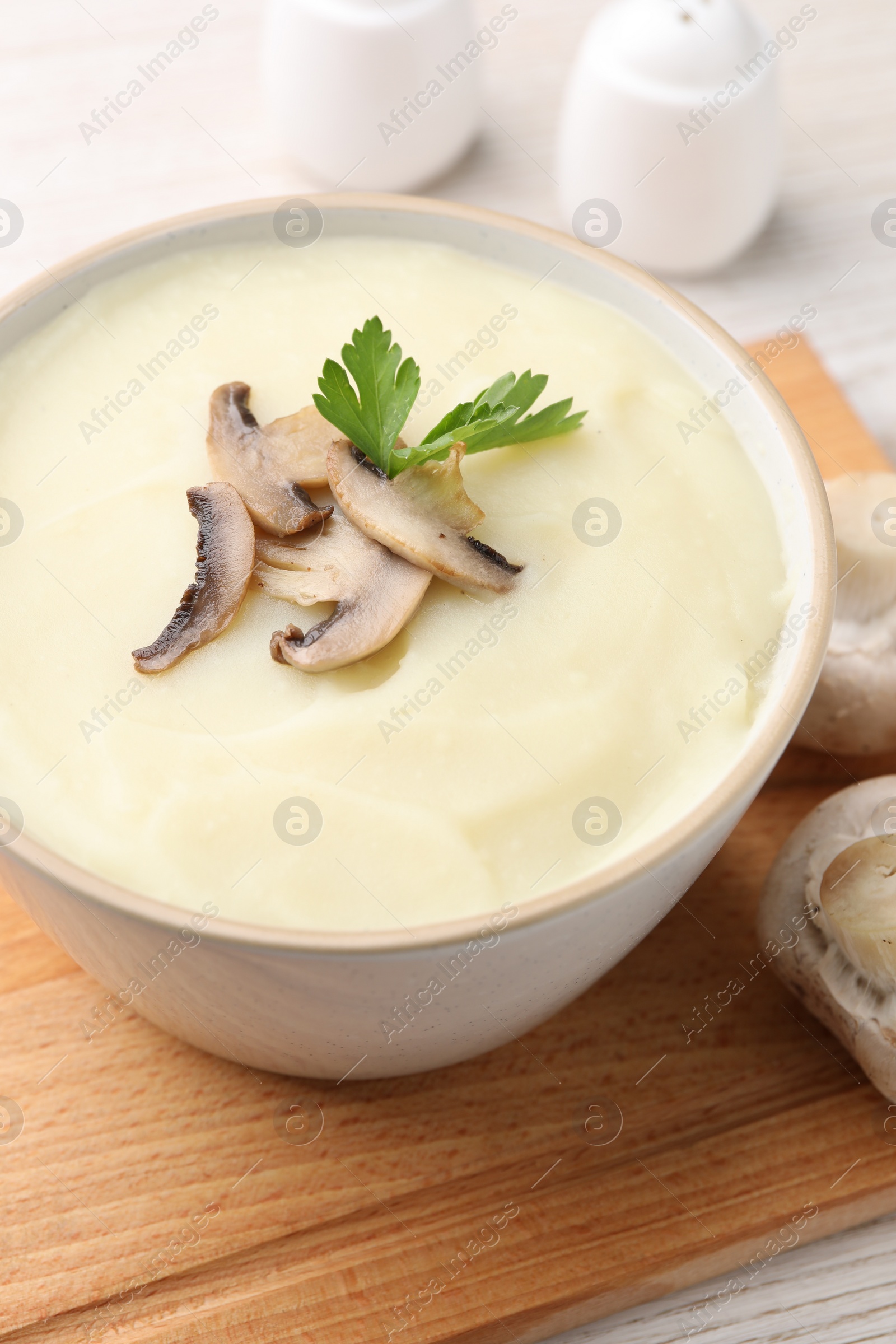 Photo of Bowl of tasty cream soup with mushrooms and parsley on light wooden table, closeup