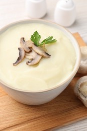 Bowl of tasty cream soup with mushrooms and parsley on light wooden table, closeup