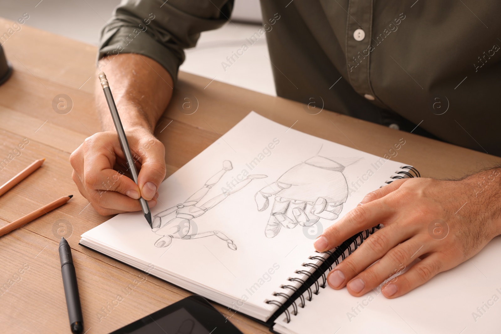 Photo of Man drawing in sketchbook with pencil at wooden table, closeup