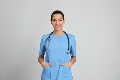 Portrait of young medical assistant with stethoscope on color background