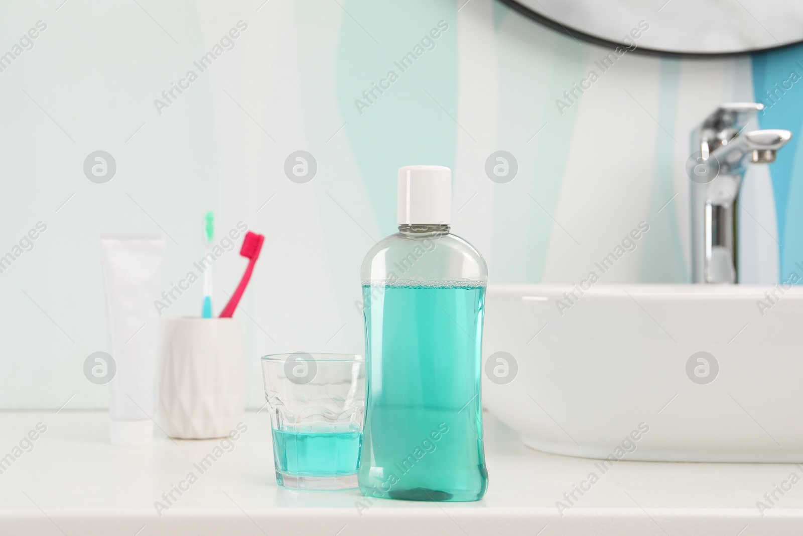 Photo of Bottle of mouthwash, toothbrushes and glass on white table in bathroom