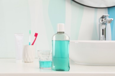 Bottle of mouthwash, toothbrushes and glass on white table in bathroom