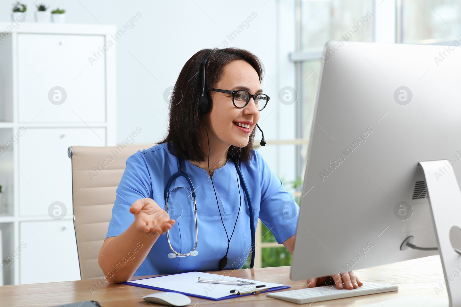 Photo of Doctor with headset and computer consulting patient online in office. Hotline service