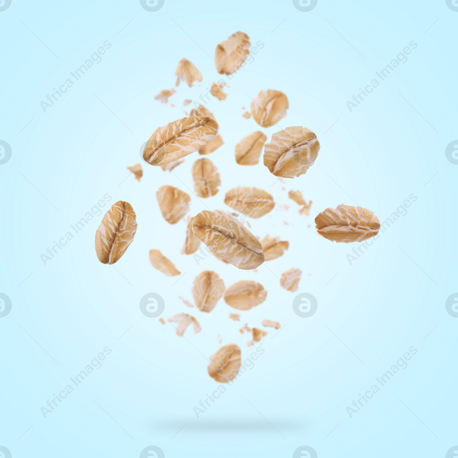 Image of Rolled oat flakes falling on light blue background