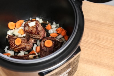 Photo of Delicious pork ribs with vegetables in multi cooker on wooden table, closeup. Space for text