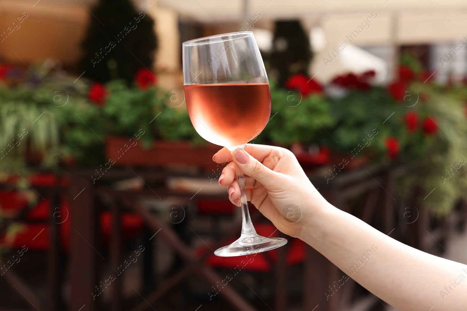 Photo of Woman holding glass of rose wine in outdoor cafe, closeup