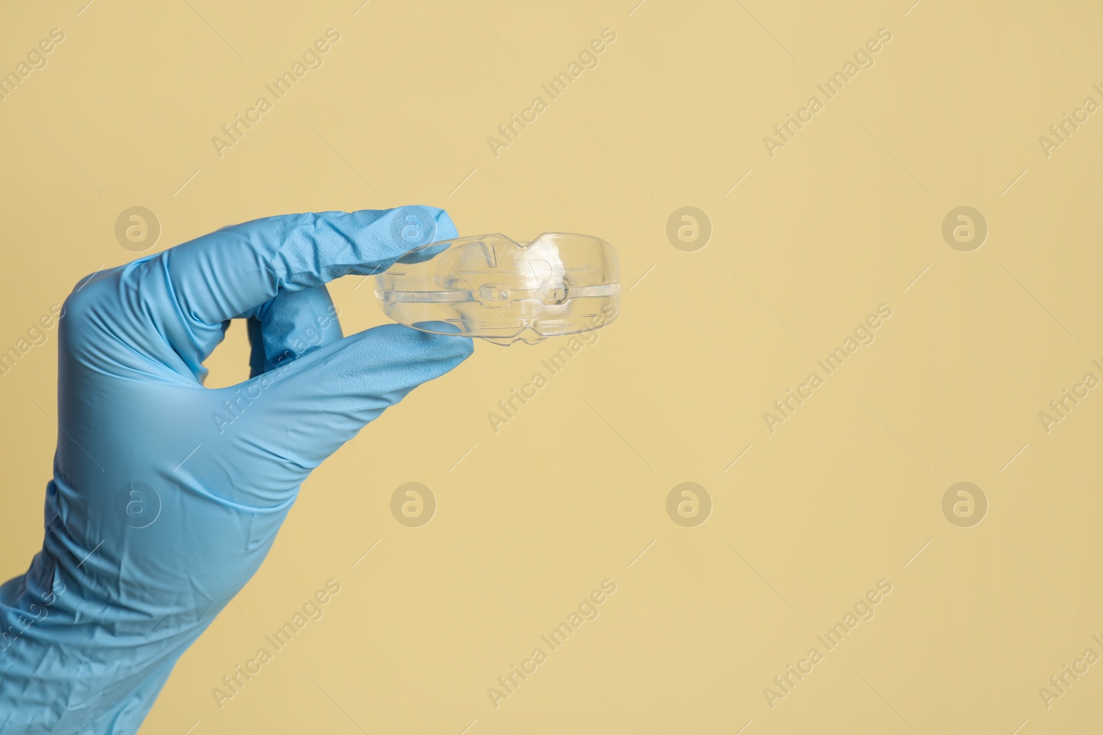 Photo of Dentist holding mouth guard on beige background, closeup with space for text. Bite correction