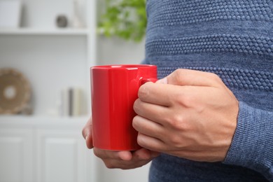 Photo of Man holding red mug at home, closeup. Mockup for design