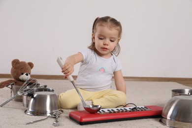 Photo of Cute little girl with cookware and toy piano at home