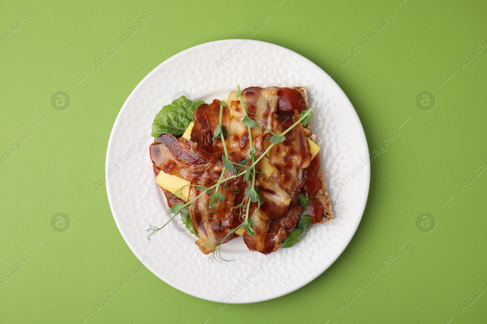 Photo of Tasty sandwich with bacon and microgreens on green table, top view