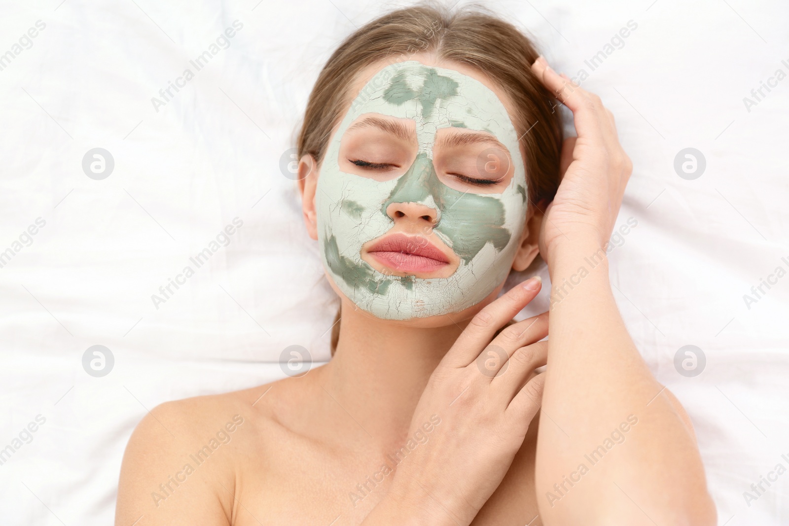 Photo of Beautiful woman with clay facial mask on white fabric, above view