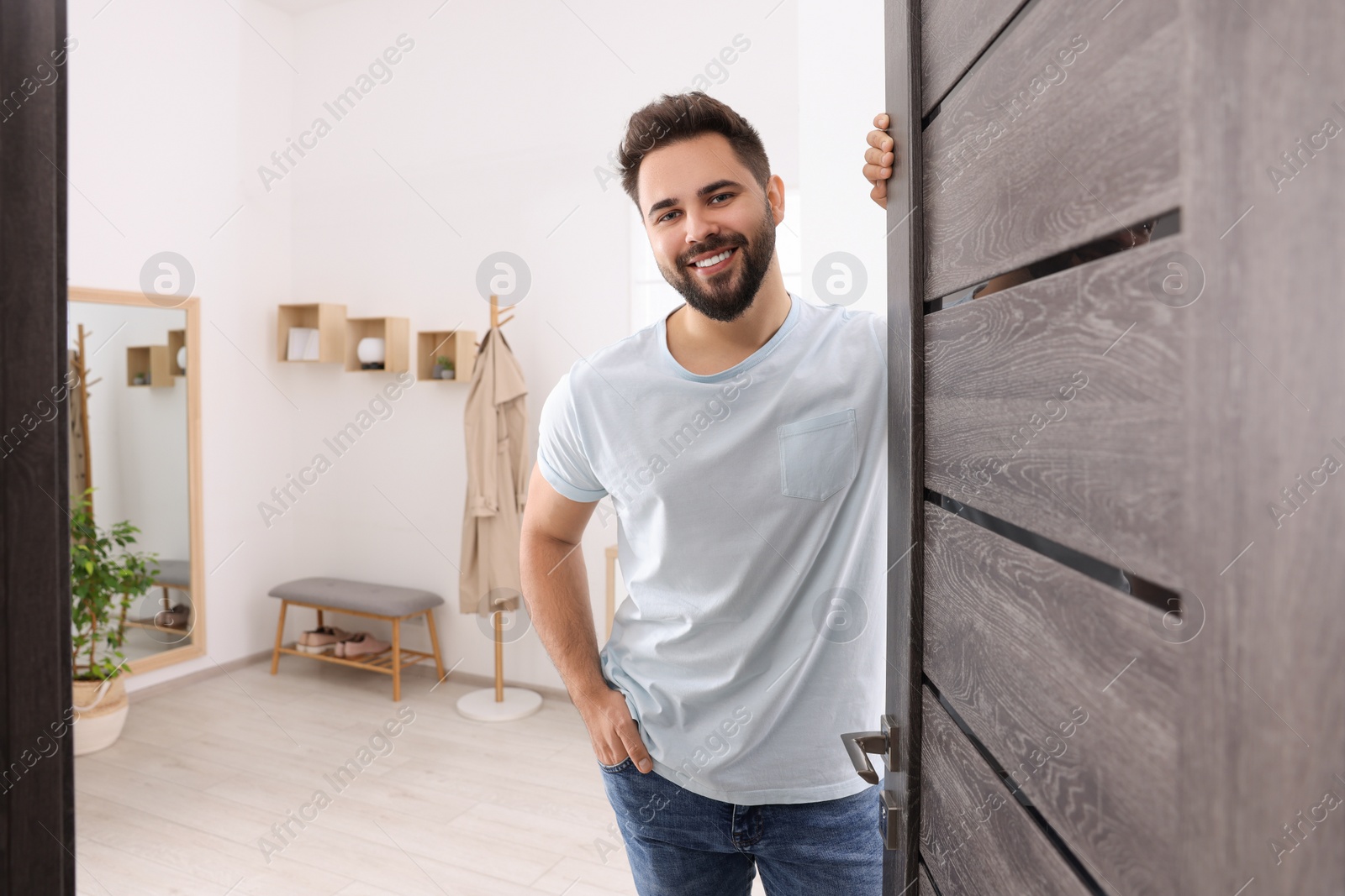 Photo of Happy man standing near door, space for text. Invitation to come indoors