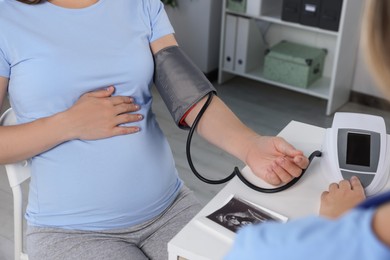 Photo of Doctor measuring blood pressure of pregnant woman in hospital, closeup