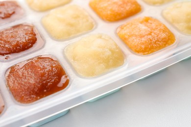 Photo of Different fruit puree in ice cube tray on white table, closeup