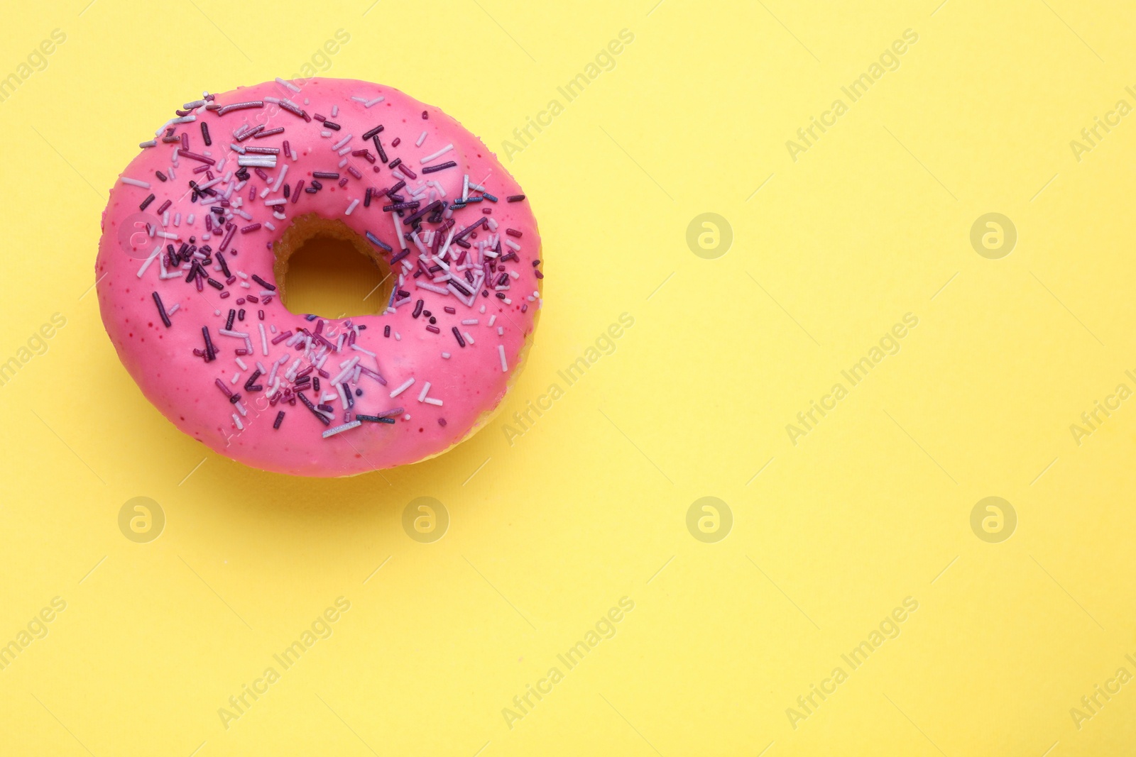 Photo of Glazed donut decorated with sprinkles on yellow background, top view. Space for text. Tasty confectionery