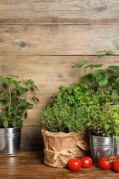 Different aromatic potted herbs and tomatoes on wooden table