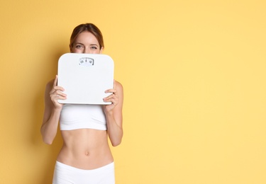 Happy slim woman satisfied with her diet results holding bathroom scales on color background