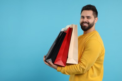 Photo of Smiling man with paper shopping bags on light blue background. Space for text