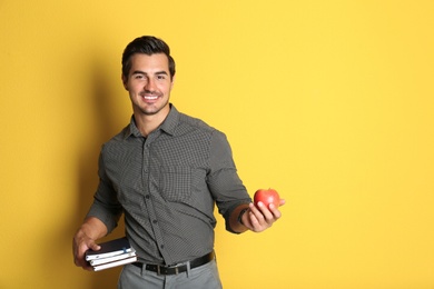 Young male teacher with books and apple on yellow background. Space for text