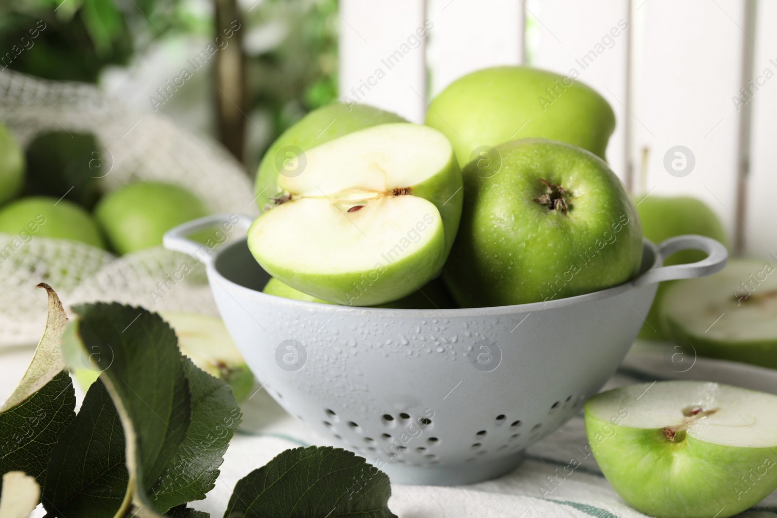 Photo of Fresh green apples with water drops and leaves on white striped tablecloth, closeup