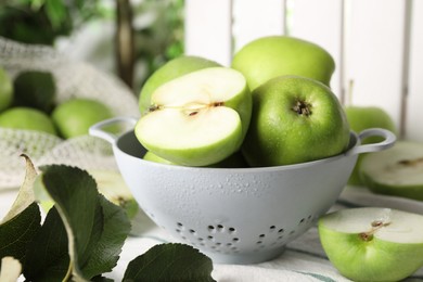 Fresh green apples with water drops and leaves on white striped tablecloth, closeup