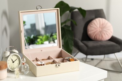 Jewelry box with many different accessories, perfumes and alarm clock on white wooden table indoors