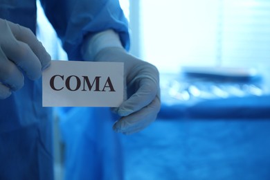 Surgeon holding card with word Coma in hospital, closeup. Space for text