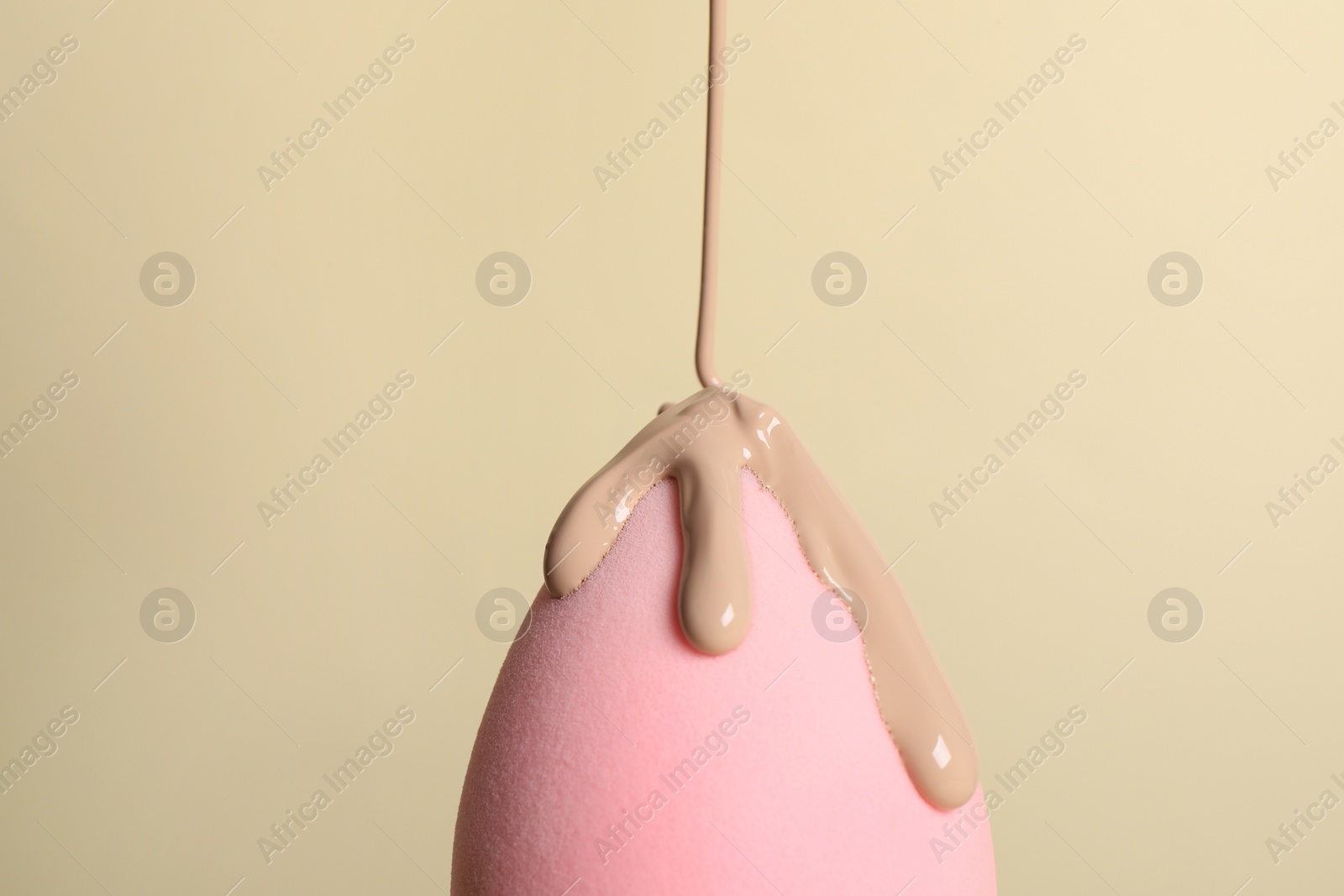 Photo of Skin foundation pouring onto makeup sponge on beige background