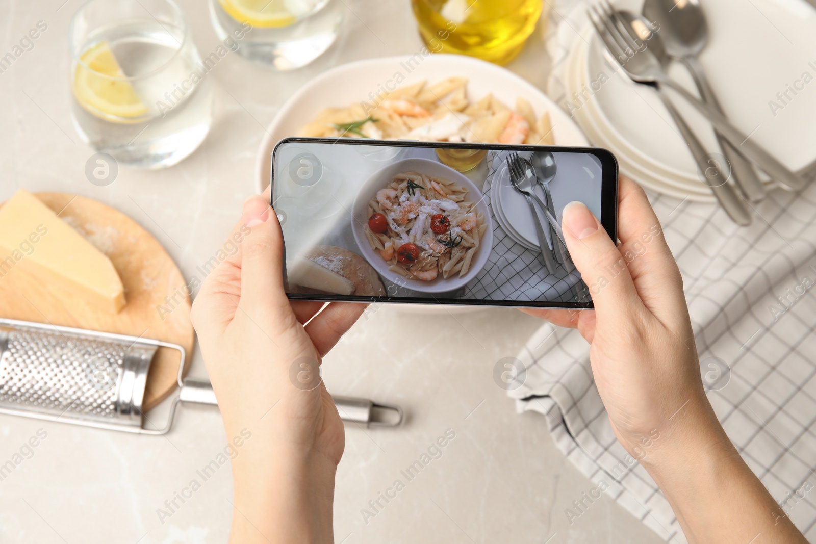 Photo of Food blogger taking picture of tasty pasta with shrimps and tomatoes at light table, closeup