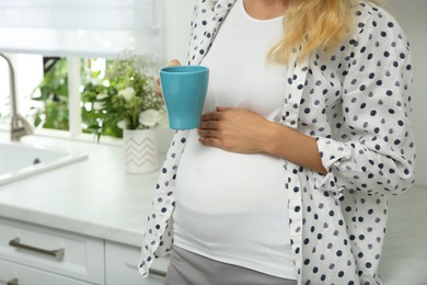 Beautiful pregnant woman drinking tea in kitchen, closeup