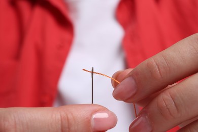 Woman inserting thread through eye of needle, closeup